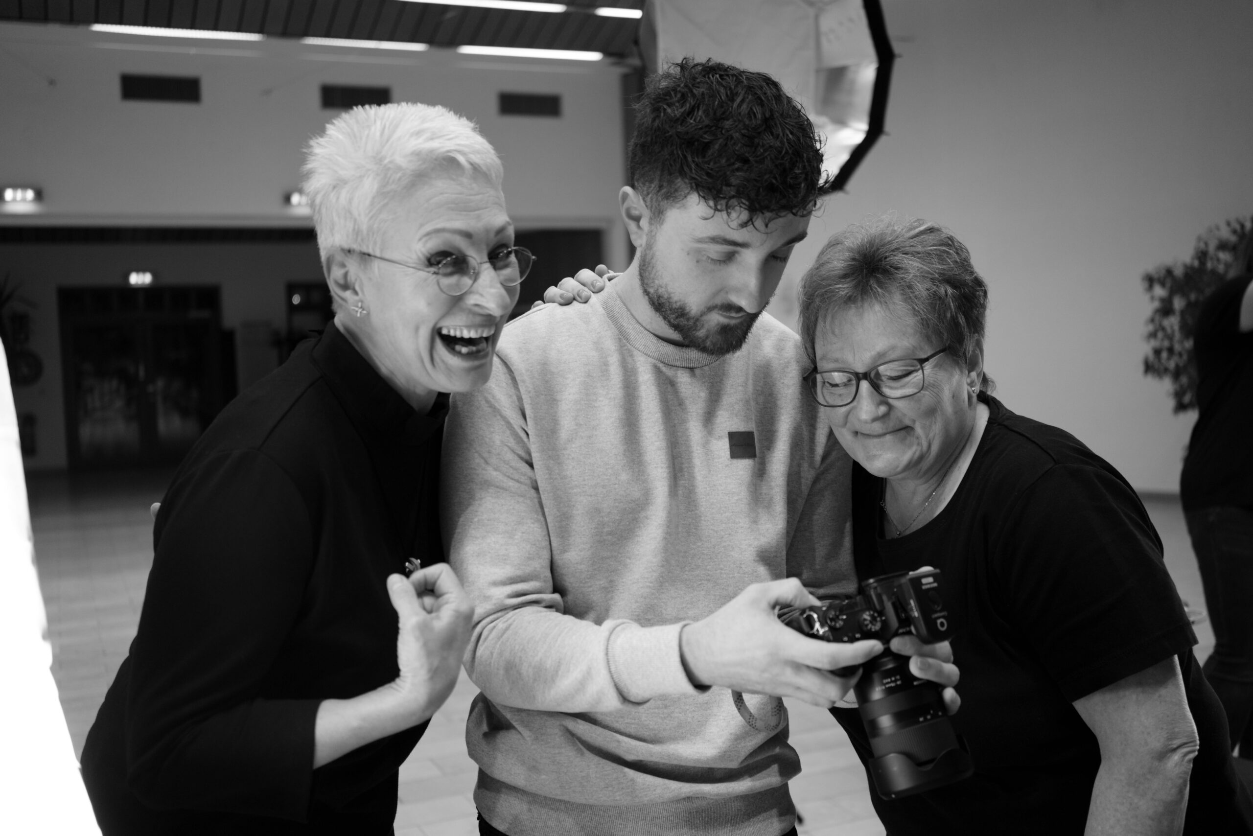 Der Eventfotograf zeigt die ersten Fotos des Events. Die beiden neben ihm stehenden Frauen lachen
