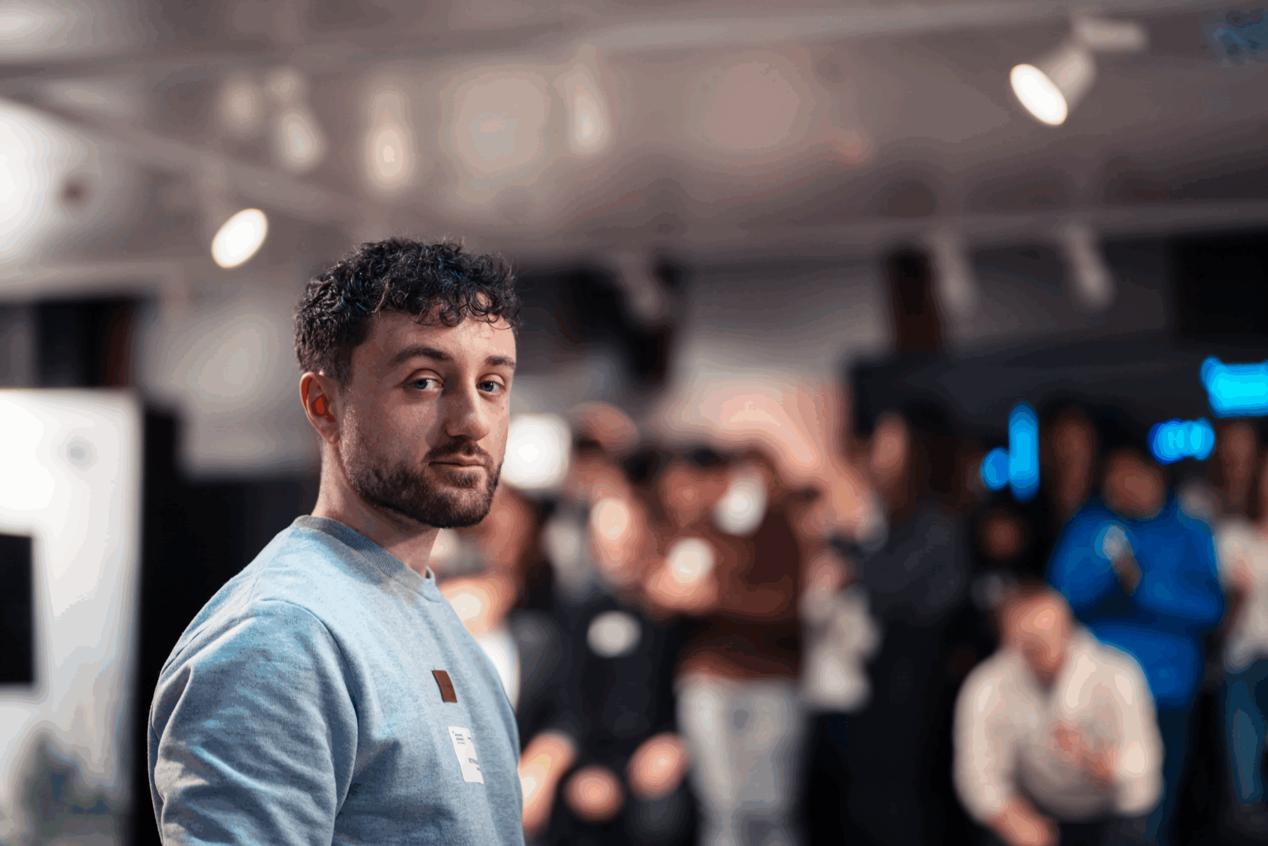 Fotograf während eines Events in Frankfurt am Main fotografiert. Er hat einen direkten blick in die Kamera, ist seitlich zu dieser gedreht, während das Event im Hintergrund stattfindet